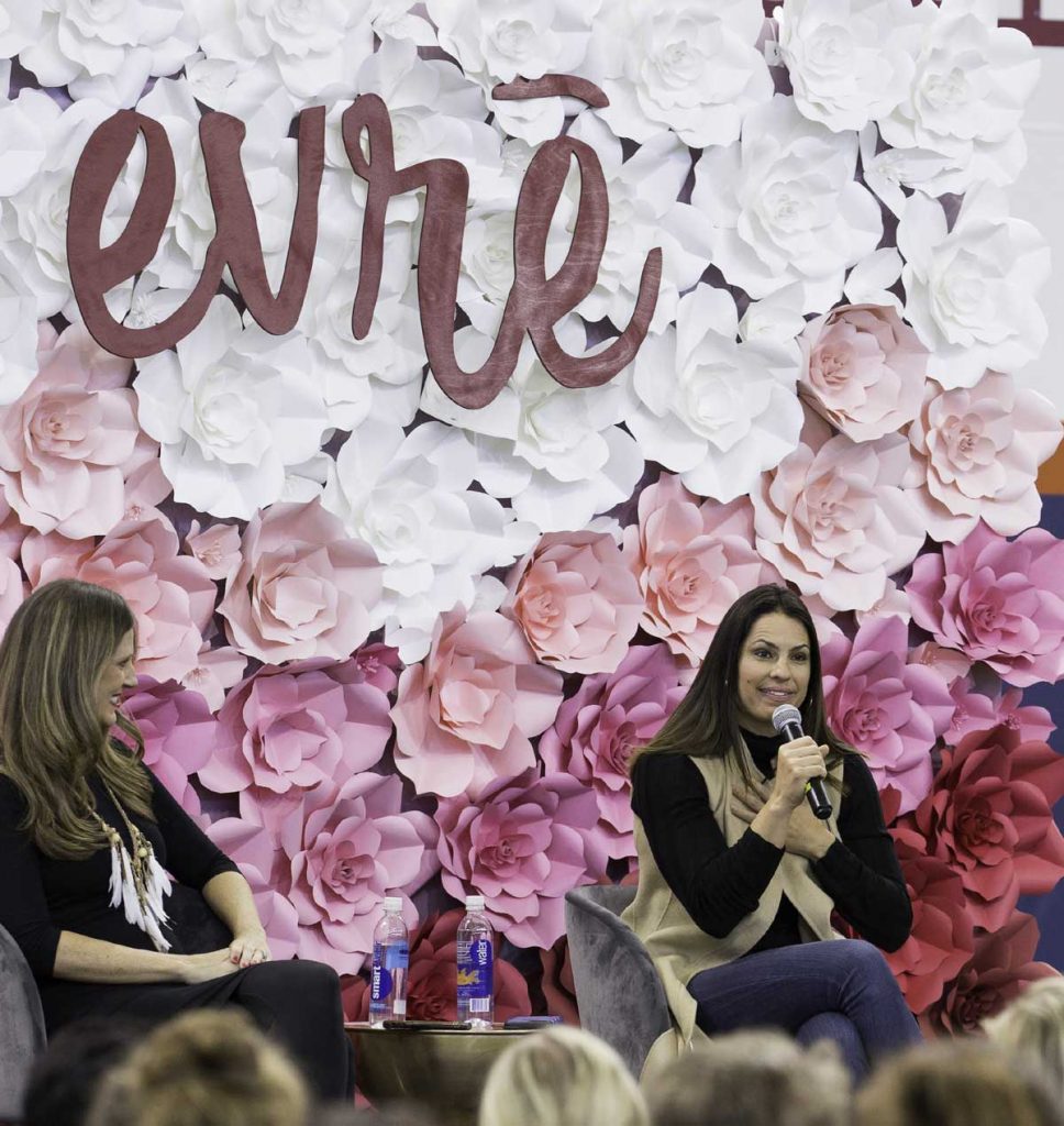 two women speak during UCHealth's womens health event called evrē. They are in front of a floral background. To the left is social media pioneer, Amy Jo Martin. To the right is ESPN baseball commentator, Jessica Mendoza.