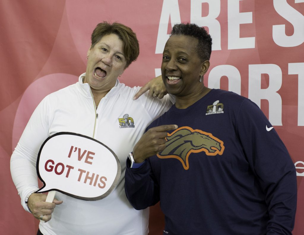 Two women pose at a photo booth. One is holding a sign that says, "I've got this."