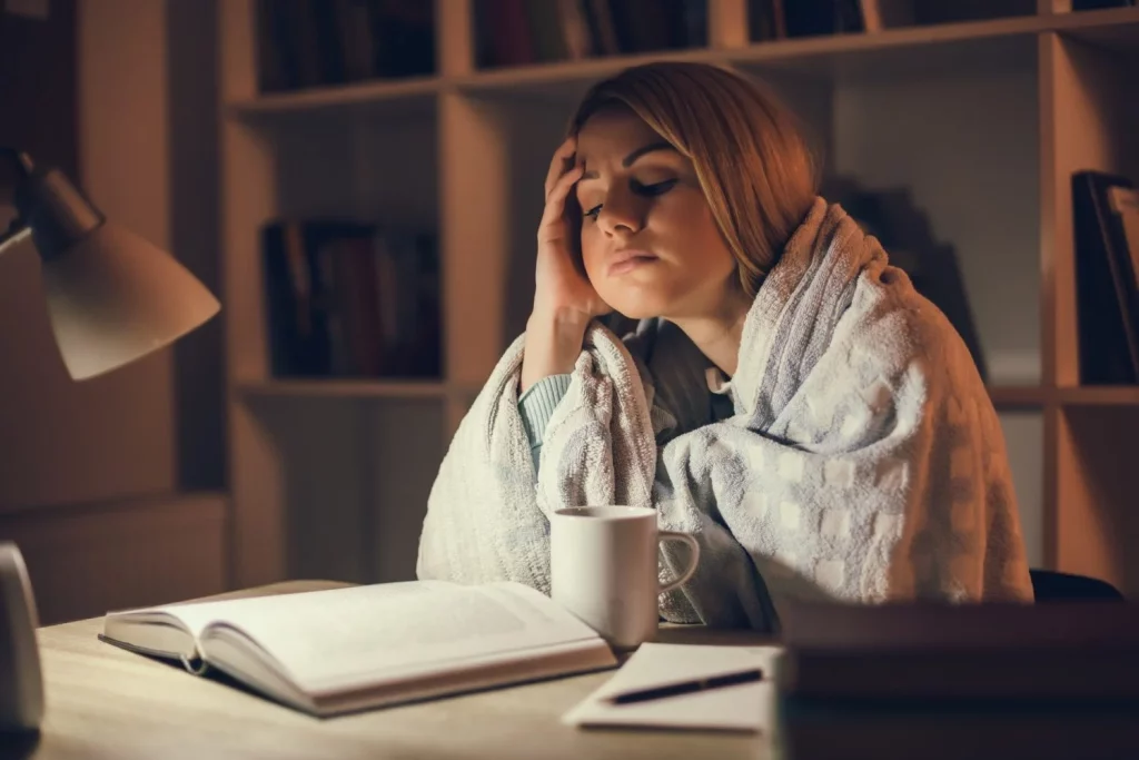 A young woman feels under the weather while trying to study, which could be bronchitis or pneumonia..