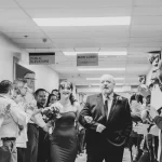 dad walks bride down long hospital hallway lined with people clapping