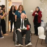 father wheeled into reception while people blow bubbles.