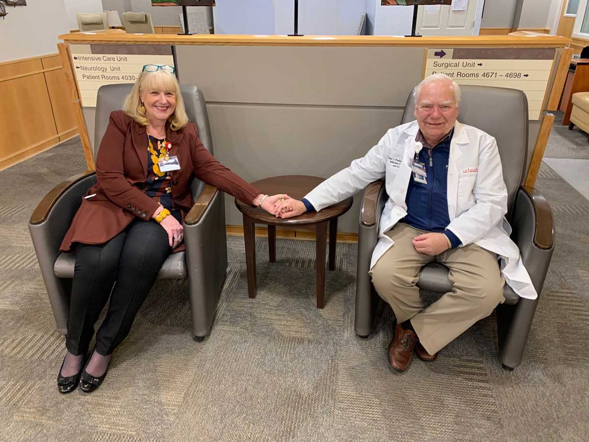 couple sits on chairs holding hands in the surgical unit waiting area