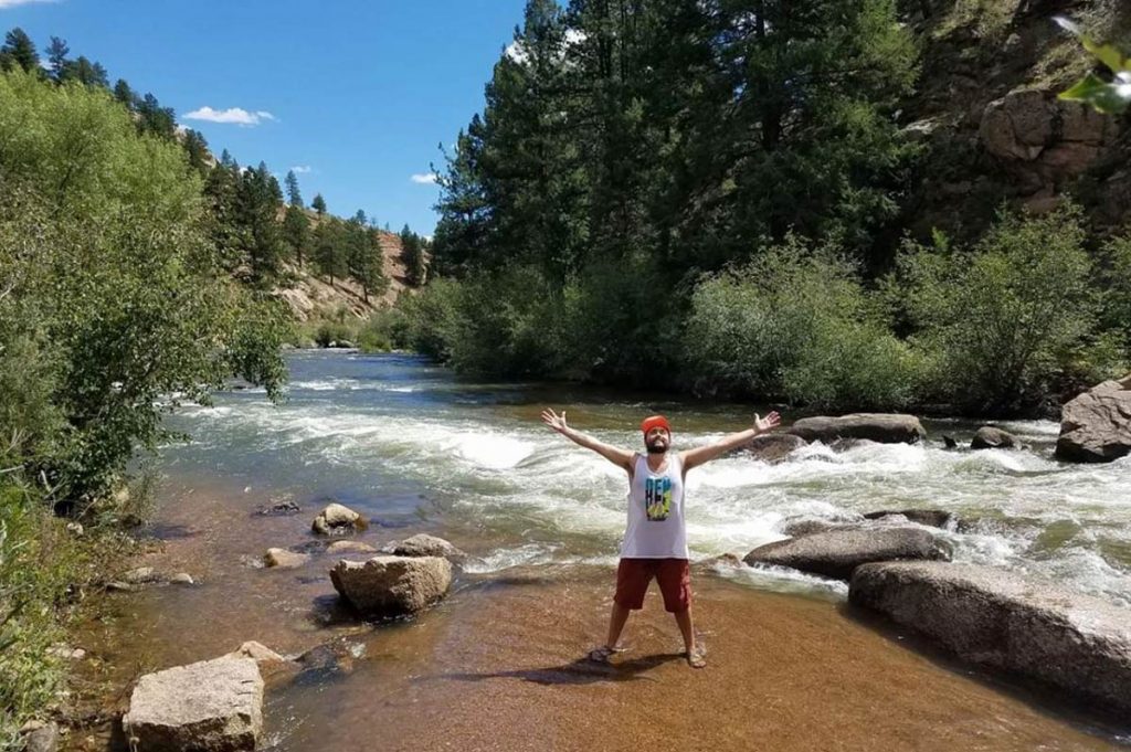 A young man stands in a river with his arms outstretched. He's celebrating life after seizures.