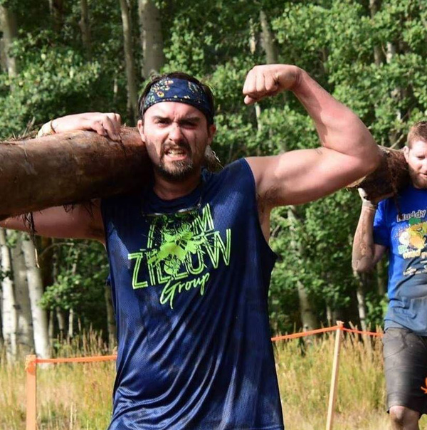 A strong guy carries a big log in a Tough Mudder compeition.