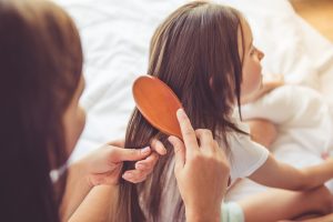 A mother brushes her daughter's hair in this image.