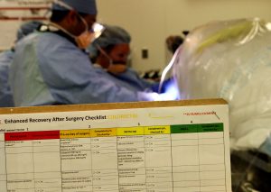 checklist held up with surgeons working on a patient in the background.