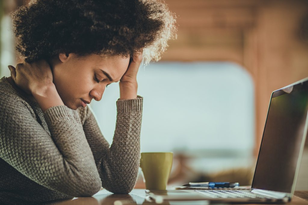 A woman holds her head after working on a laptop.