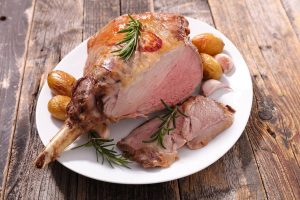 a rosted leg of lamb on a white platter with roasted potatoes