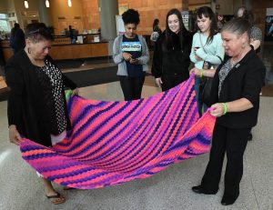 Sara Millard and Ruth Sena admire a blanket that Sena made for Millard. It's purple with orange and blue.