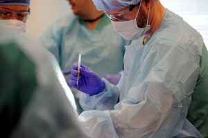 man in operating room suit holding a needle