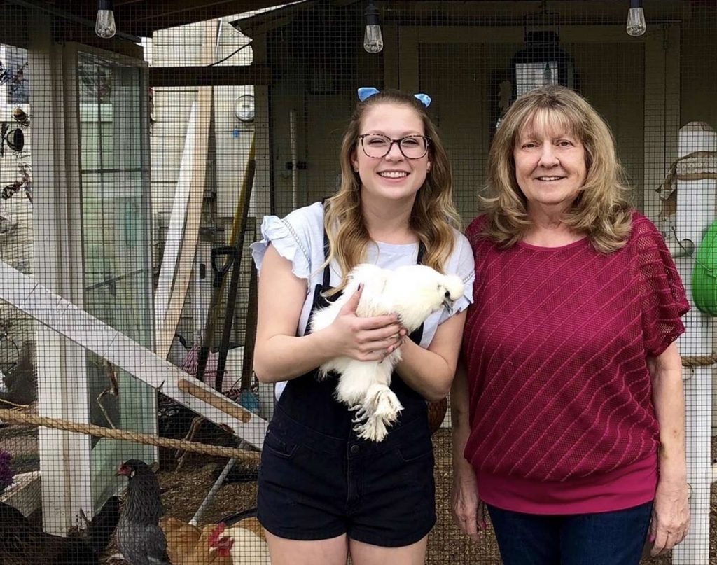 A daughter holds a chicken as she stands next to her mom outside their chicken roost.