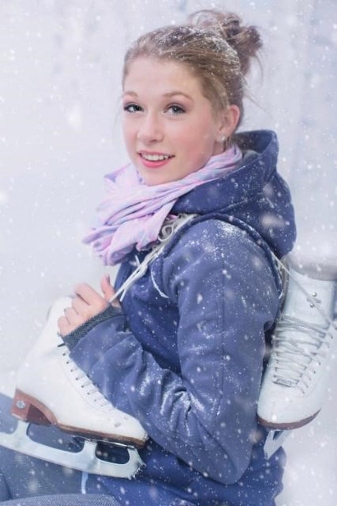A young woman poses with figure skates over her shoulders.