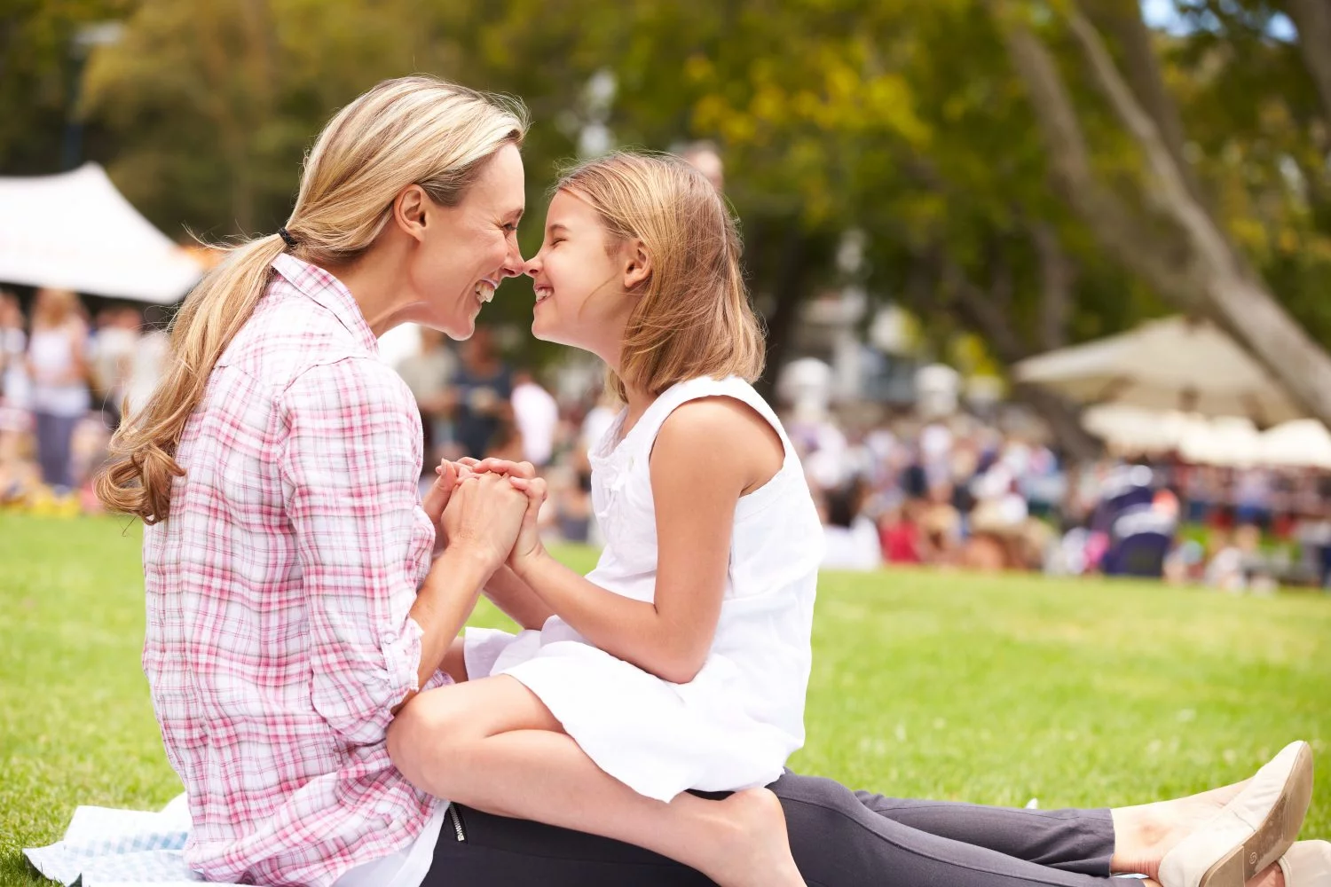A mom and daughter smile at each other in a park.