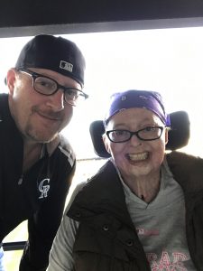 Jamie and Troy Ketchum pose at a Colorado Rockies game. She is in a wheel chair after surviving terrible burns. But she continues to smile.