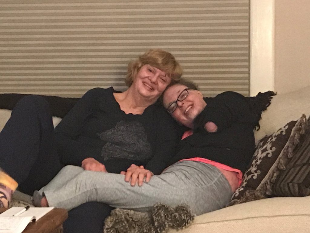 A woman who suffered terrible burns and lost both legs and an arm after a car crash hugs her mom as they pose on a couch.