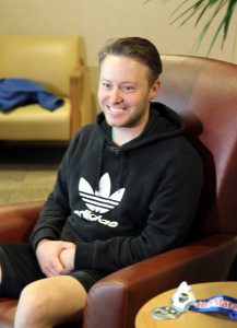 Kyle smiling, sitting in a chair with his running medal next to him.
