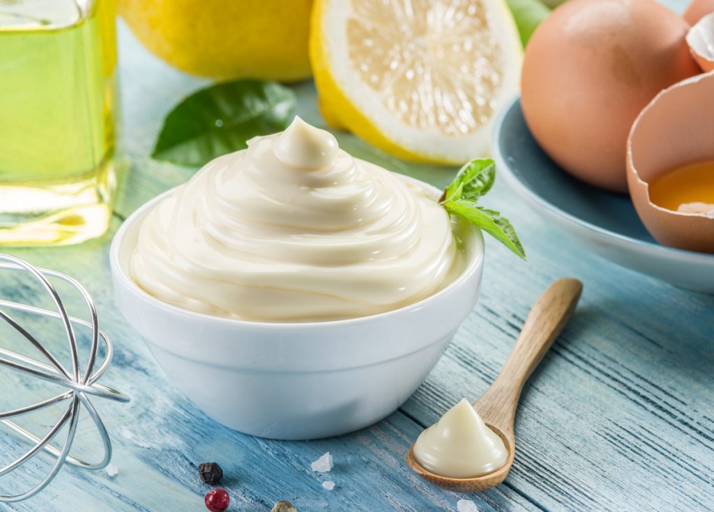 homemade mayonnais with a bowl surrounded by egss and lemons
