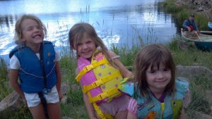 Girls giggle as they were their lifevests near a lake.