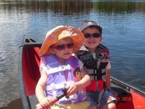 Two little boys rowing a canoe on a lake.