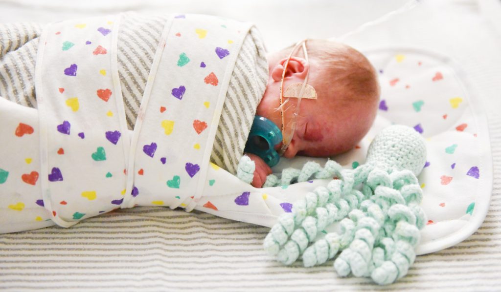 A preemie baby grabs onto an octopus tentacle that a volunteer knitted for preemie babies.