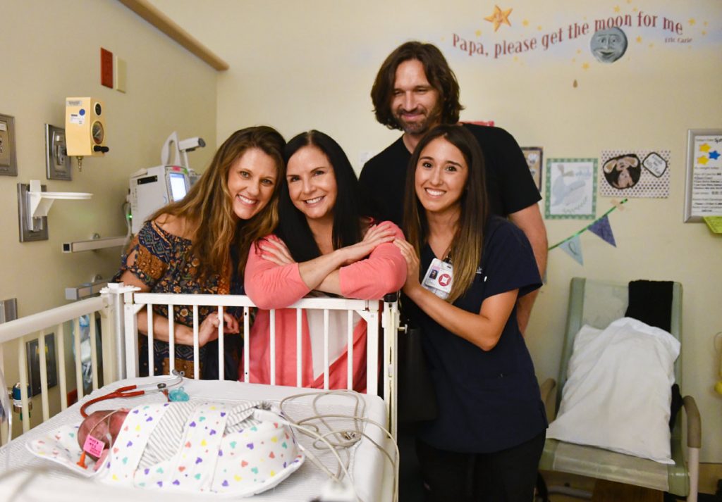 A preemie baby in his crib with his parents and two of his nurses.