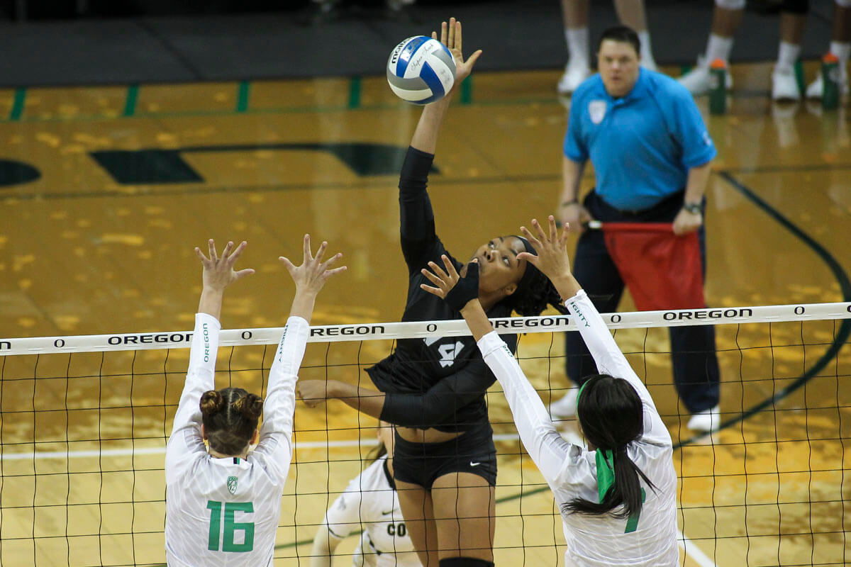 two payers blocking while Abu spikes the volleyball in a game after her meniscus surgery