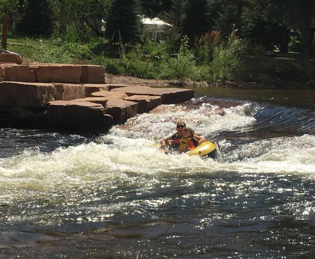 woman and child going down a rapid in Colorado summer tubing river.