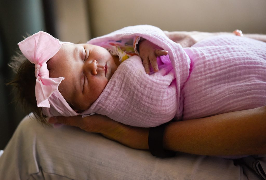 a newborn baby snoozes wearing a pink bow. Wrapped in a pink blanket, Eloise Burford was the first baby born in Highlands Ranch, CO