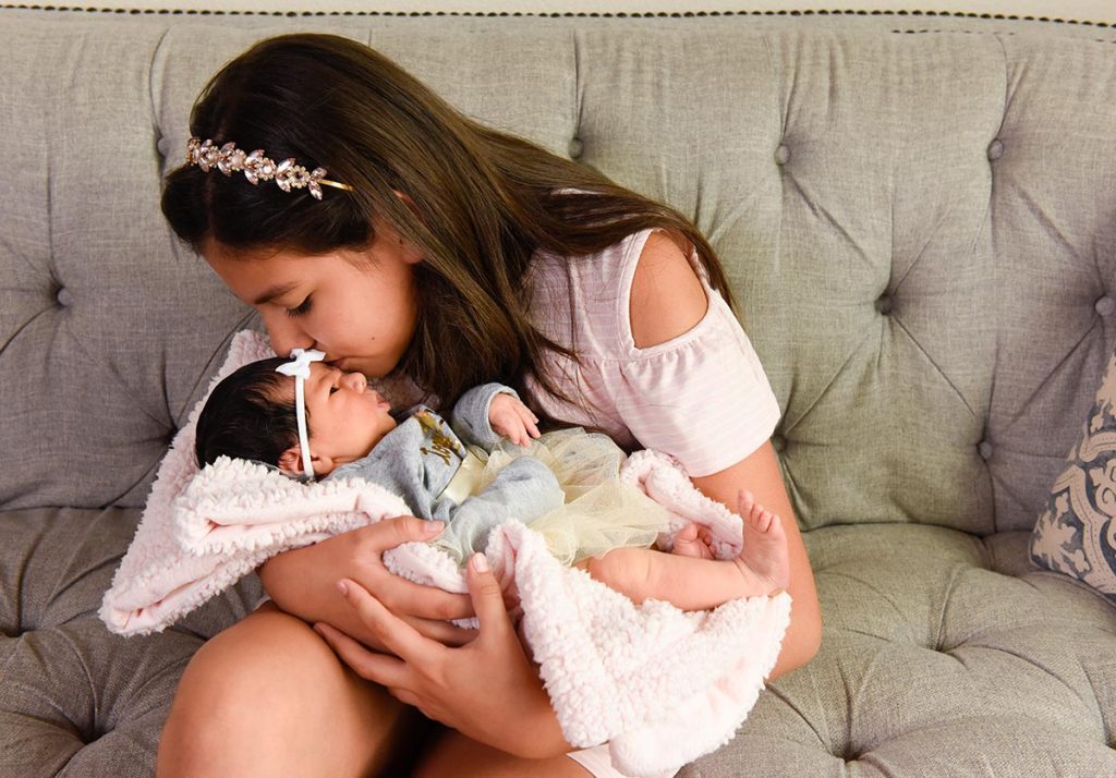 A 10-year-old kisses her new baby sister.