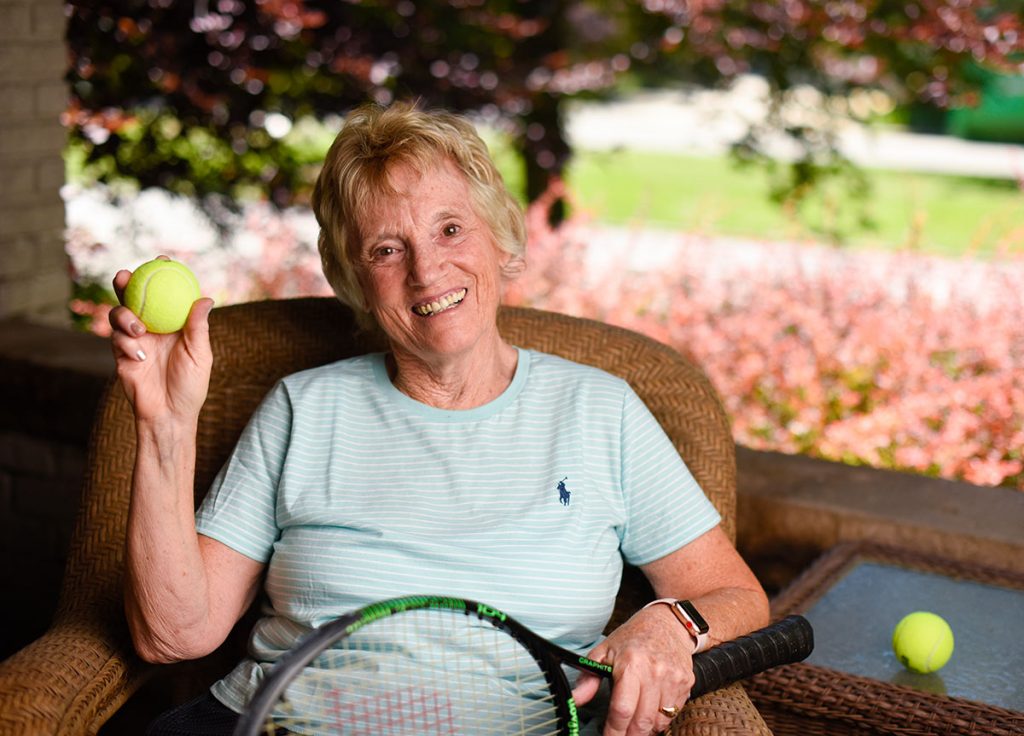 Susan High suffered a torn hamstring while playing tennis. She poses on her front porch in Denver with a tennis ball and racket.