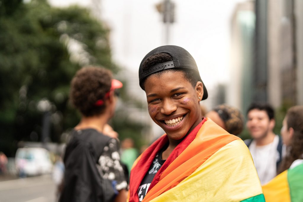 a teen boy with a Pride flag wrapped around his shoulders