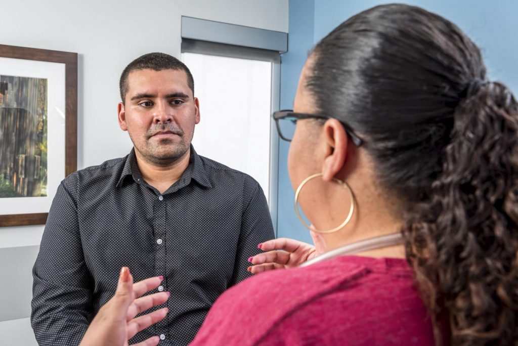 A care provider talks with a gentleman at a doctor's office. UCHealth is dedicating more than $100 million to enhance behavioral health care in Colorado. Clinical social workers will work alongside primary care physicians to help patients with behavioral health care needs.