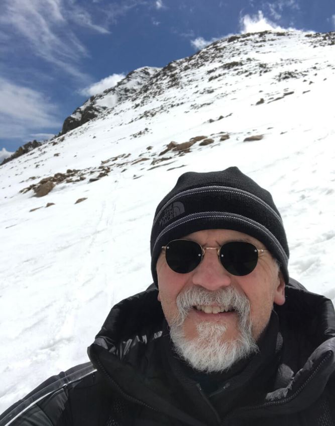 Dr. Corky Dillon on Mt. Bierstadt after surgery for a rare lung illness. This shows a headshot with snow on the peak behind him.