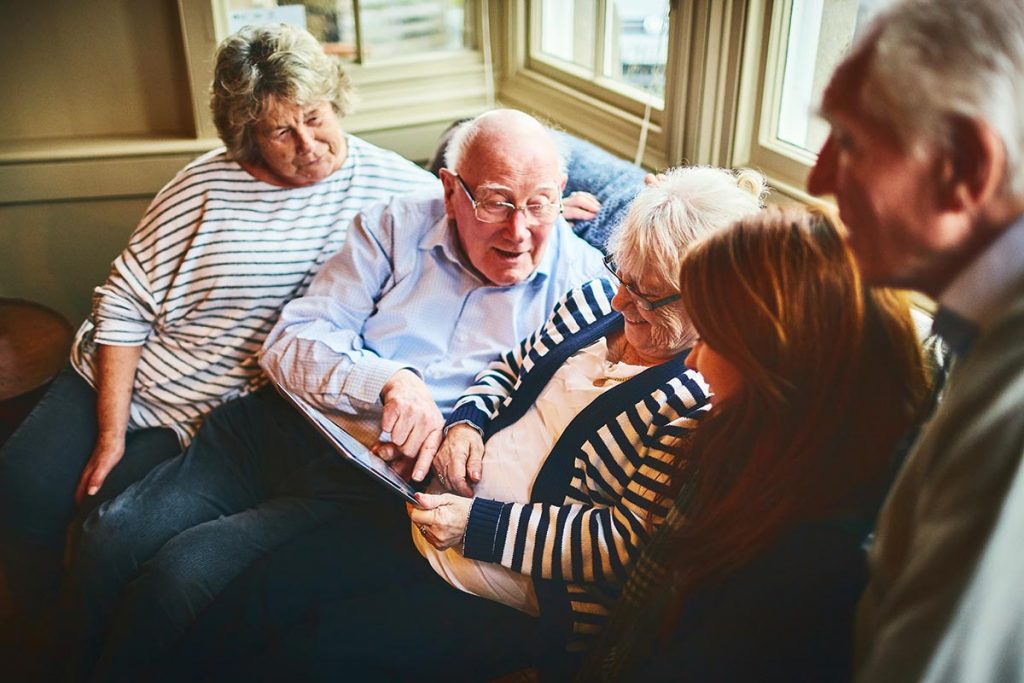 A family gathers around an elderly woman who is holding a tablet to illustrate palliative care telehealth.