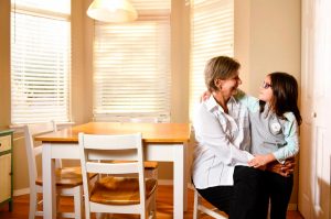 grandmother looks into grandaughter's eyes as she sits on her lap at the kitchen table.