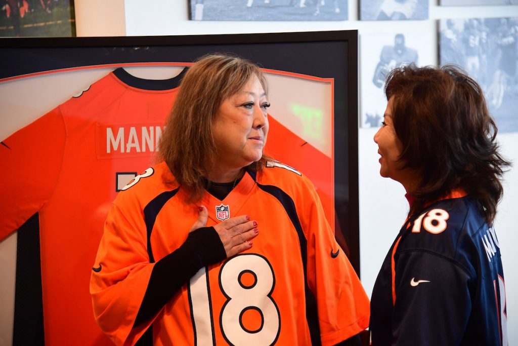Linda Regis holds her hand over her chest as she wears a Denver Broncos jersey and talks to the mother of her lung donor.