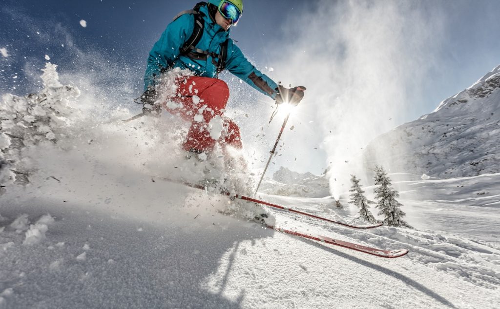 An alpine skier goes down a sunny ski slope in this photo.