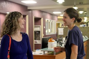 Two women, a former patient and nurse, laugh together in an ICU corridor. The patient returned to thank hospital staff for her care.