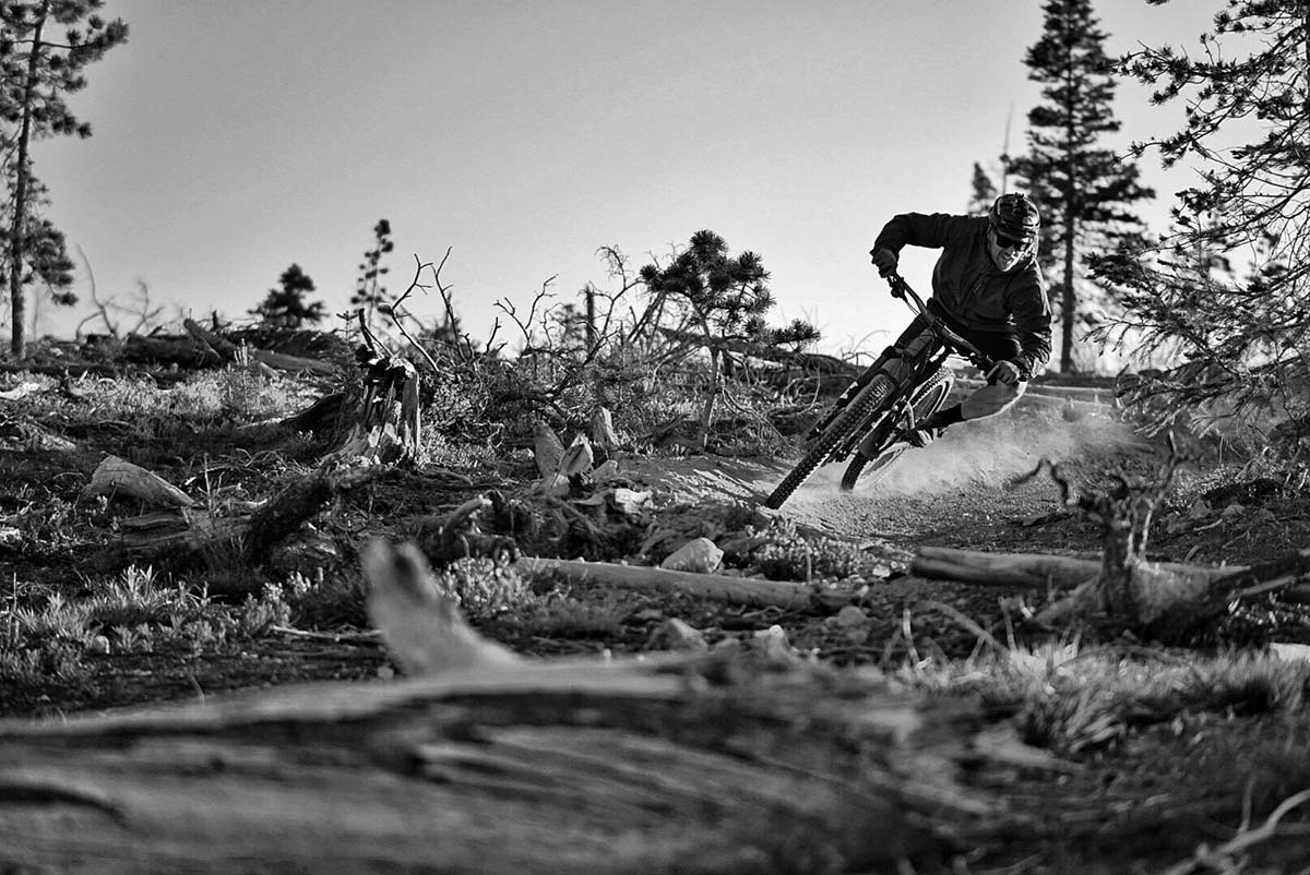 black and white photo of a mountain biker speeding around a corner on a dirt alpine track.