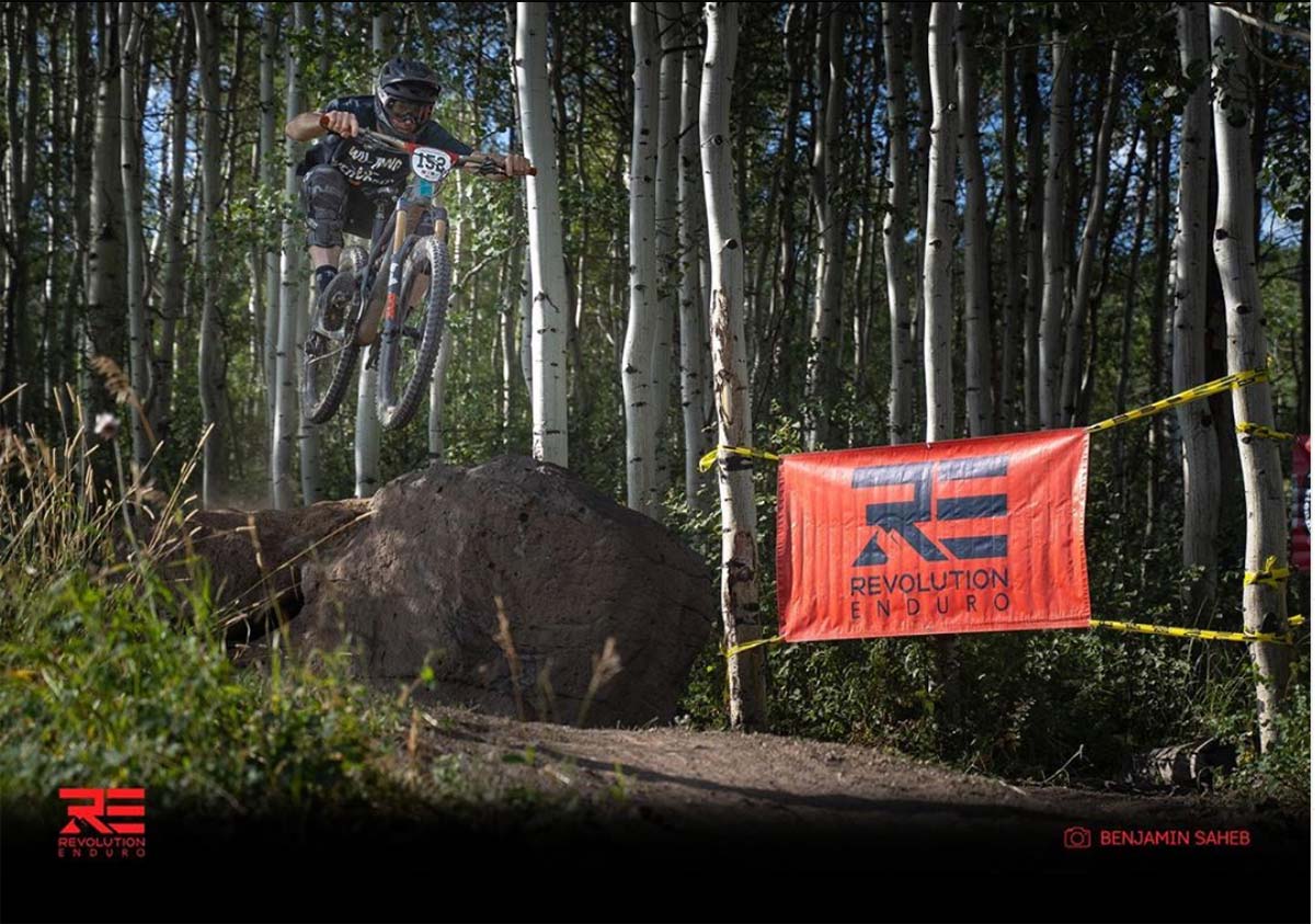 mountain biker leaps off a jump during a wooded race.