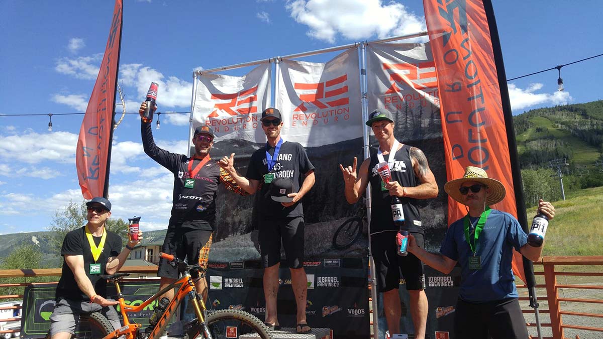 Three mountain bikers standing on an outdoor stage with their trophies.