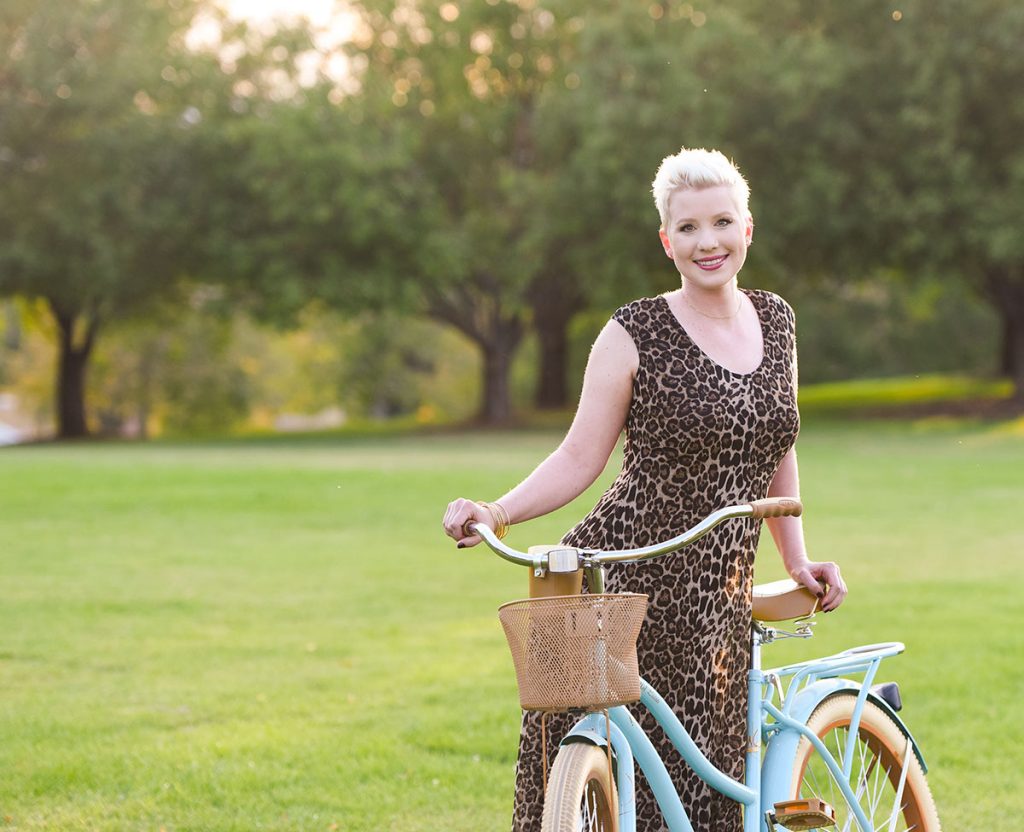 melanoma survivor Lauren Race poses with her blue cruiser bike at a Denver Park. She speaks out now about the dangers of tanning.