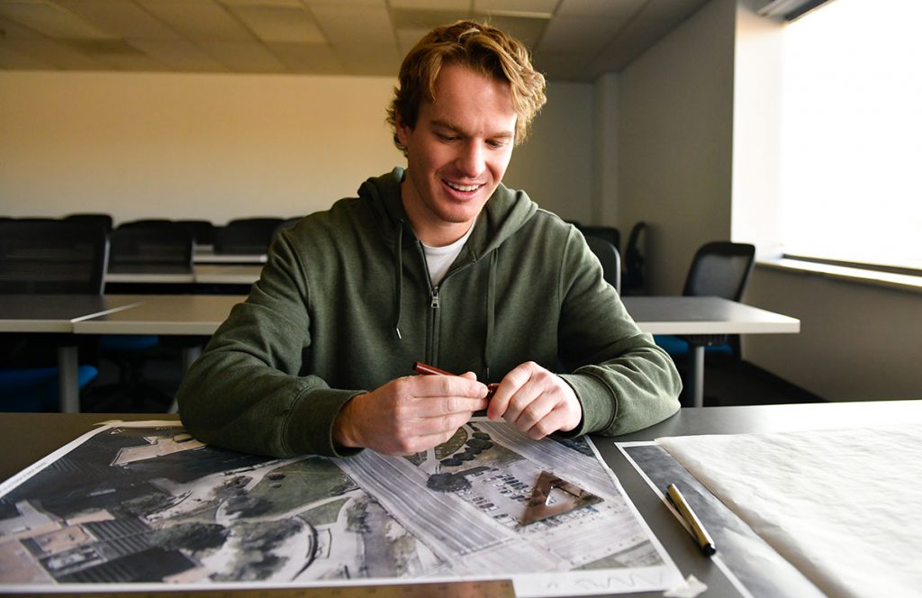 Jon Blank looks over an aerial image of the nearby Creekfront Park, along Cherry Creek at Larimer Street. He is creating a new design for the park for one of his graduate classes at University of Colorado Denver. He is in an empty classroom on campus.