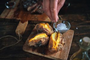 a hand sprinkling rock salt on baked potatoes