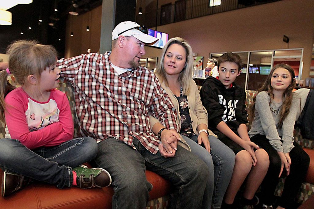 The alexander family sit on a bench for family bowling night, being able to return to the fun event months after Keith, the father, was diagnosed with colon cancer.