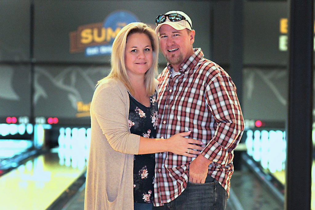 dawn holds her husband for a photo in front of the bowling lanes.