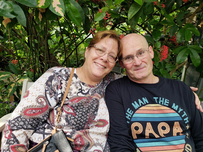 couple poses together on bench in front of bushes