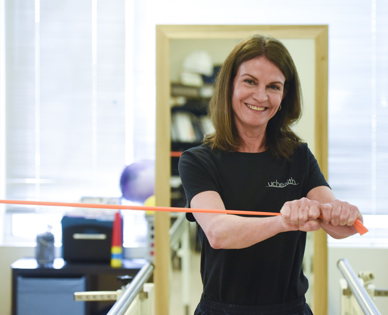 Woman looks at camera as she uses an exercise band with her arms.