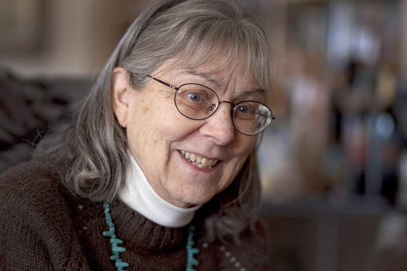 Woman with classes, turquoise necklace and turtleneck smiles.