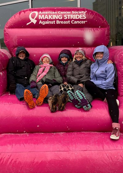 five adults sit on a big inflatable pink couch at breast cancer event.